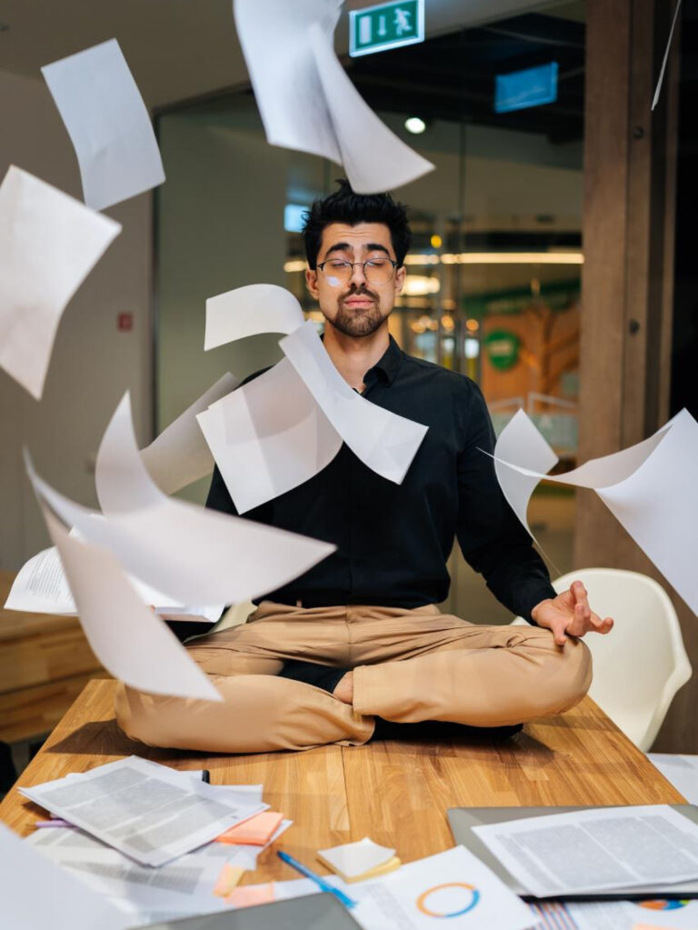 How Eastern Practices Naturally Restructure Your Busy Western Life Man Sitting in Meditation Pose With Papers Dropping Around Him